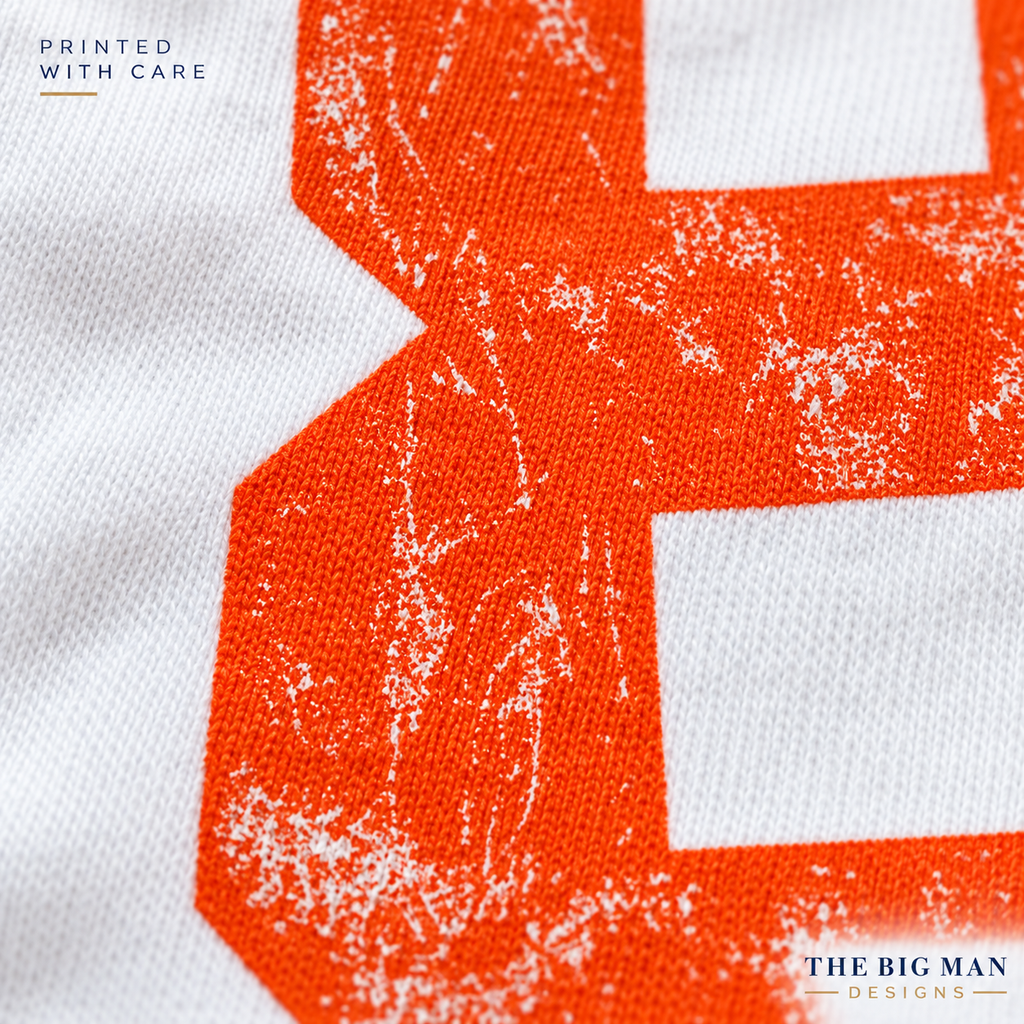 Close-up of distressed orange number printing and cotton knit texture on a white garment. The Big Man Designs.