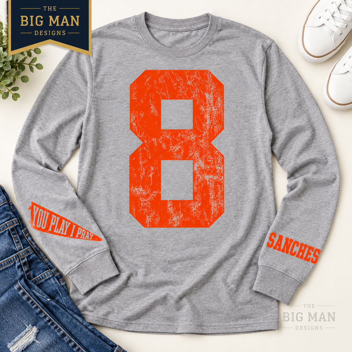 Gray long-sleeve shirt flat lay with orange distressed number 8 and small wrist prints: YOU PLAY I PRAY pennant and sample SANCHES name.