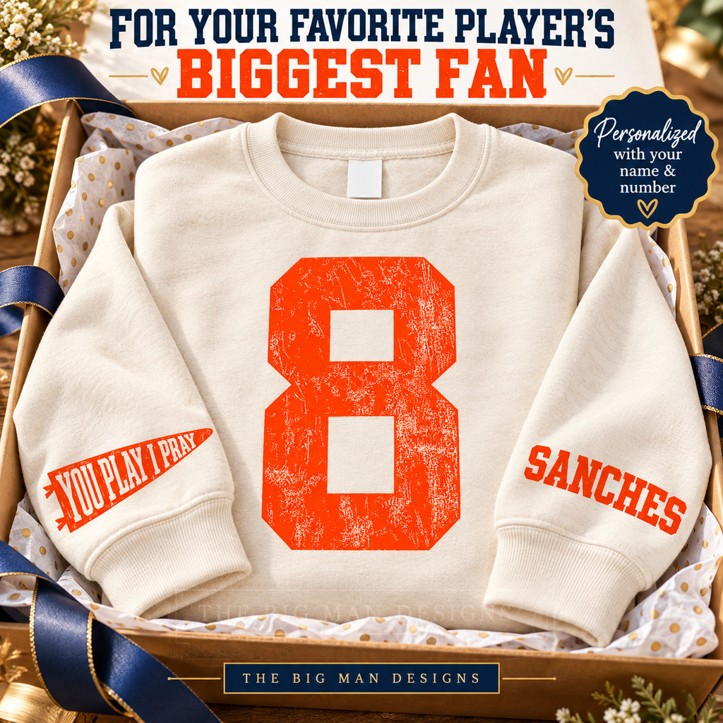 Natural personalized number sweatshirt in gift packaging, displaying the front 8, YOU PLAY I PRAY pennant and sample SANCHES wrist name.