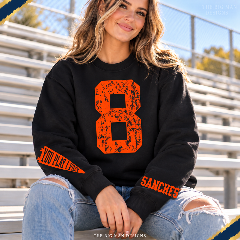 Black personalized sweatshirt worn at sports bleachers, orange distressed number 8 and wrist prints, showing a sample custom SANCHES name.