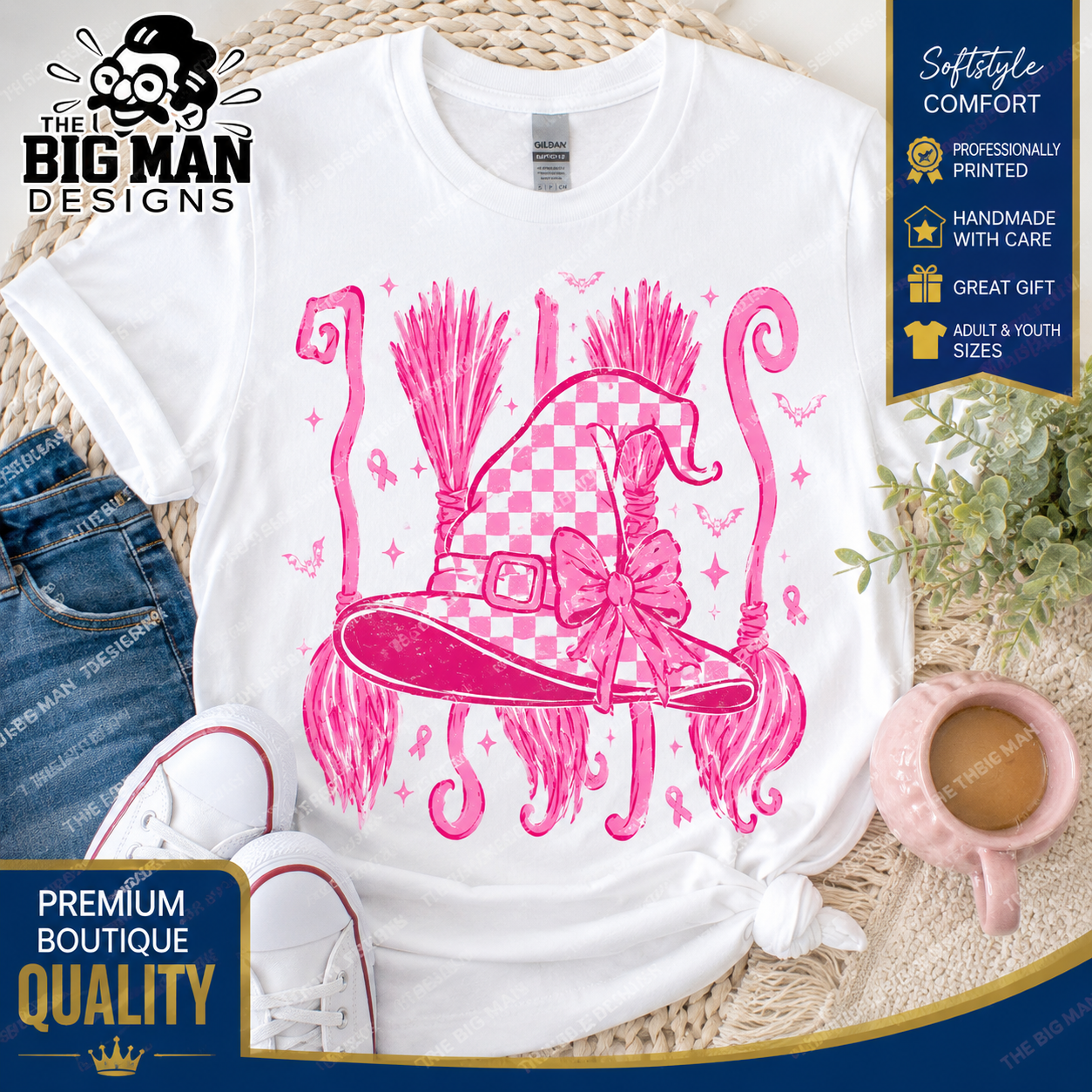 A white graphic t-shirt featuring a pink witch hat design with a checkered pattern, bow, and broomsticks. The t-shirt is styled in a flat-lay arrangement with blue jeans, white sneakers, a pink mug, and a wicker mat, with promotional badges from 'The Big Man Designs' visible.