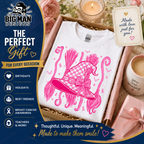 A white crewneck t-shirt featuring a bright pink graphic of a witch hat with a checkered pattern, presented inside a gift box with candles, flowers, and a mug. The left side has a dark blue promotional banner for 'The Big Man Designs' gift set.
