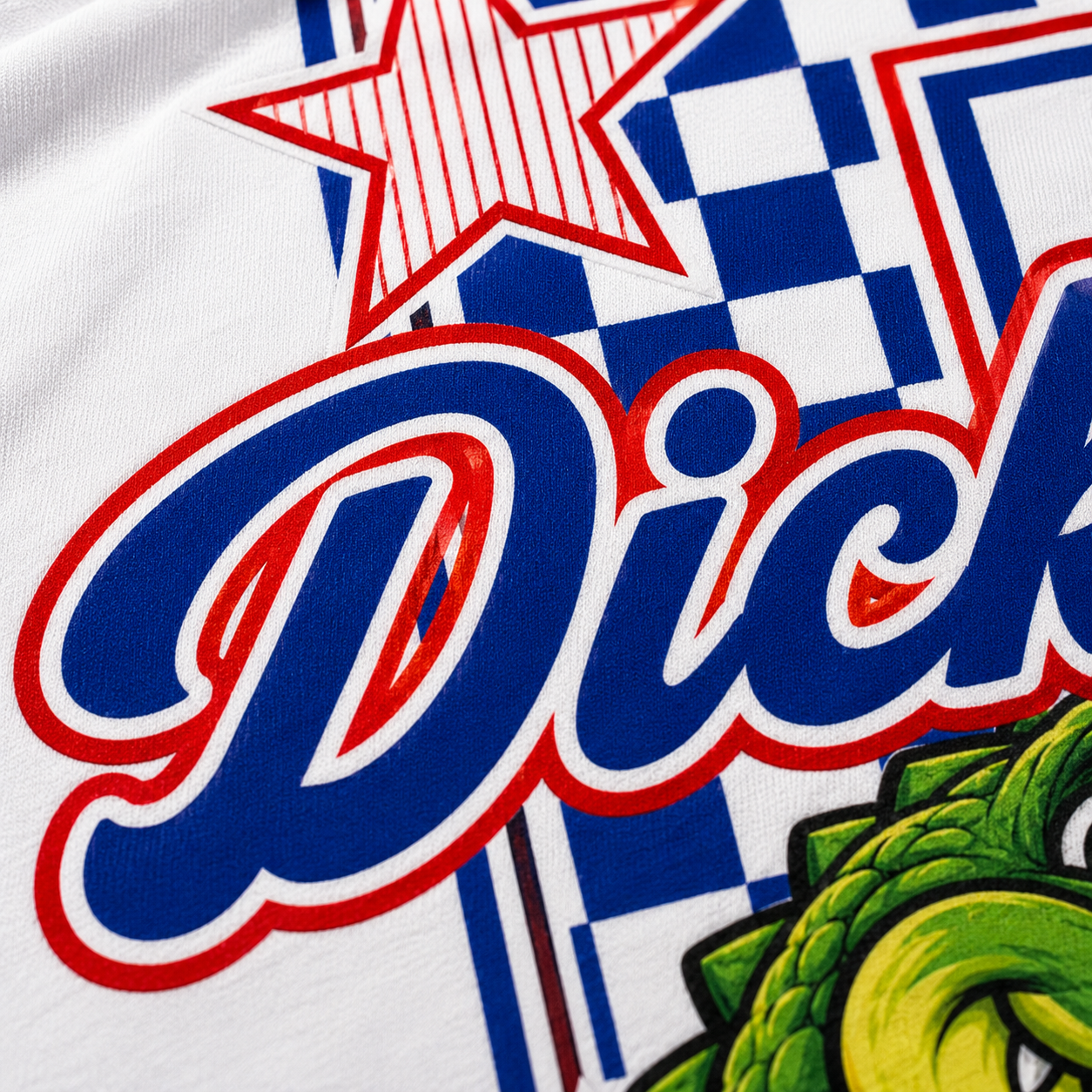 Close-up of a white graphic t-shirt featuring a blue and red checkered pattern, a red and white striped star, large blue cursive text outlined in red, and a green cartoon gator graphic.