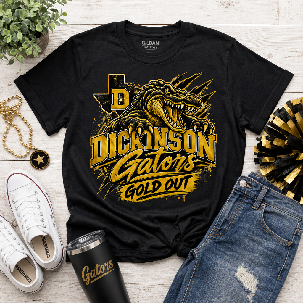 A black Gildan t-shirt with a gold and yellow graphic of a gator and the text 'DICKINSON Gators GOLD OUT', styled in a flat lay with white sneakers, blue jeans, a black tumbler, a gold chain, and a plant on a white wood background.
