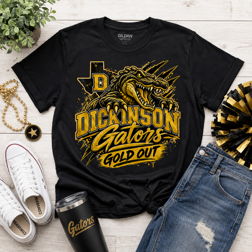 A black Gildan t-shirt with a gold and yellow graphic of a gator and the text 'DICKINSON Gators GOLD OUT', styled in a flat lay with white sneakers, blue jeans, a black tumbler, a gold chain, and a plant on a white wood background.