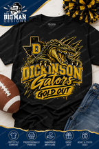 A black short-sleeve graphic T-shirt laid flat with a football, jeans, and a pom-pom around it. The shirt features a large gold and yellow alligator design with the text 'DICKINSON GATORS GOLD OUT' and a Texas-shaped letter D.