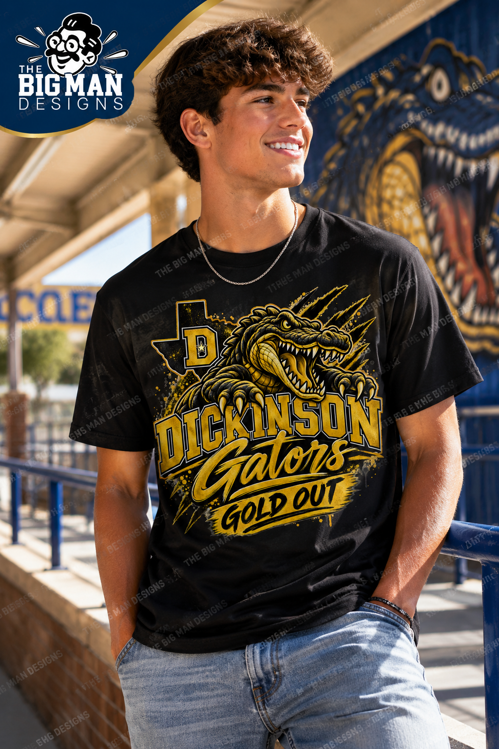A smiling young man wearing a black graphic t-shirt with a gold and yellow alligator design and the text 'DICKINSON Gators GOLD OUT'. The background shows a blue brick walkway and a large blue alligator mural.