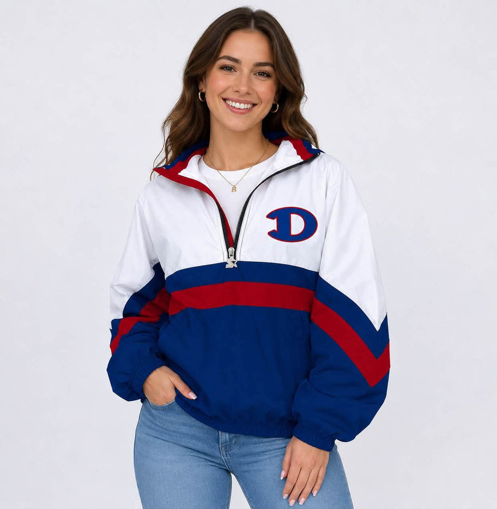 A woman wearing a white, navy blue, and red color-blocked half-zip jacket with a large navy and red 'D' logo on the left chest, paired with light blue jeans, against a plain white studio background.