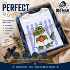 A white T-shirt folded inside a gift box with blue tissue paper, tied with twine, and presented in a styled promotional layout. The shirt has a cartoon ghostly green alligator holding an orange mug.