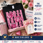 A curated gift set for breast cancer awareness featuring a black t-shirt with a pink football graphic, a pink tumbler, a thank you card, a gift box, and a heart-shaped ornament, arranged in a styled flat-lay with promotional text overlays.