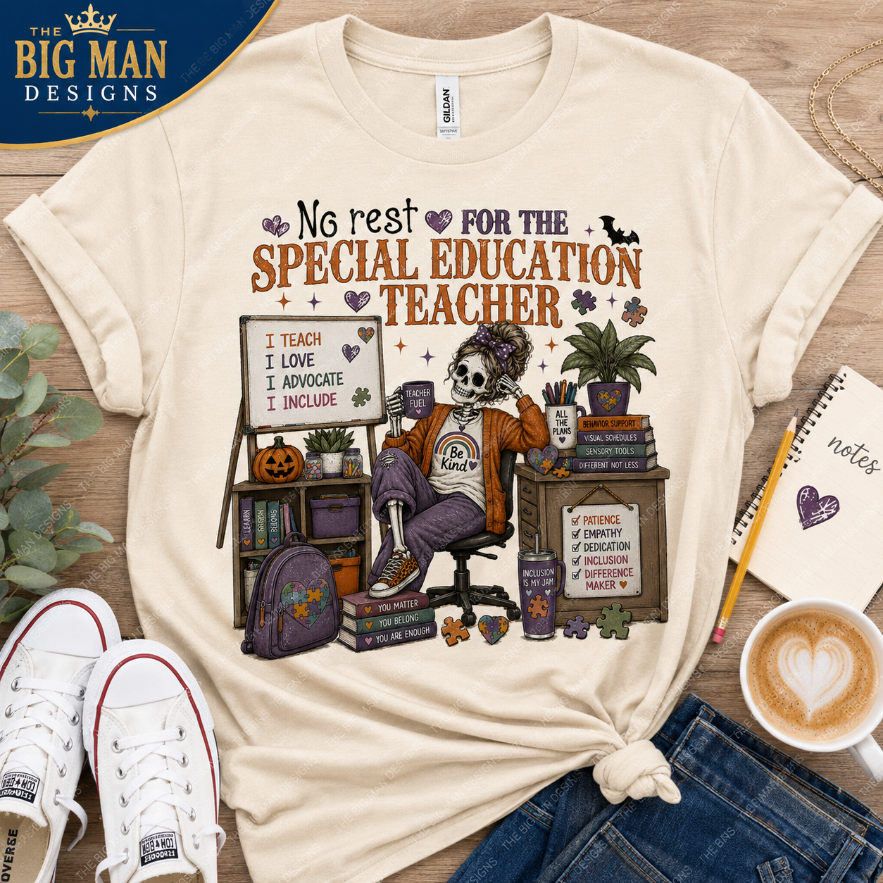 A cream-colored graphic t-shirt featuring a Day of the Dead skeleton teacher sitting at a desk with books and a chalkboard. The t-shirt is styled in a flat-lay arrangement on a wooden surface with jeans, sneakers, a coffee cup, and a notebook, with a 'The Big Man Designs' logo in the top left corner.