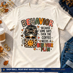 Natural teacher humor T-shirt with messy bun, leopard coffee cup, and behavior plan wording styled with jeans and coffee.