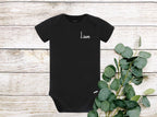A black baby onesie with short sleeves and the name 'Liam' embroidered on the front in white thread.