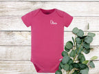A pink baby onesie with short sleeves and a white embroidered name 'Olivia' on the front.