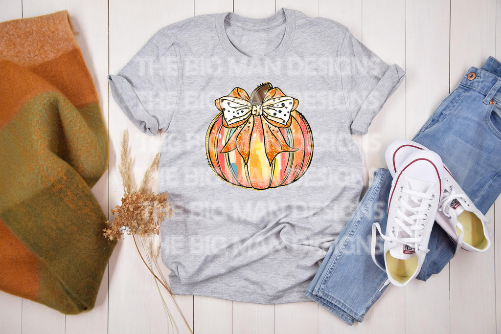 A cozy fall t-shirt featuring a brushstroke pumpkin with a faux glitter effect and a coquette bow. This trendy fall shirt is made from 100% cotton and available in sport grey, natural, black, and white. Perfect for a pumpkin patch outfit, Thanksgiving outfit, or a cute autumn aesthetic. The premium DTF print ensures durability with no cracking or peeling. A must-have for cottagecore and neutral fall fashion lovers! available on grey, black, white, and natural.
