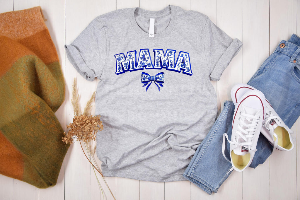 Elegant & timeless! This blue and white Chinoiserie-inspired “Mama” design features intricate floral details and a delicate coquette bow, creating a sophisticated, vintage aesthetic. Perfect for sublimation, DTF transfers, and DIY projects like t-shirts, sweatshirts, tote bags, mugs, and more! on grey