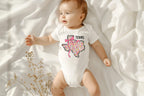 Dress your little one in Texas charm with a coquette twist! This adorable State Floral Coquette Texas design features a hand-drawn Texas silhouette adorned with delicate florals for a soft, vintage-inspired Western aesthetic. Whether for rodeo season, Texas pride, or everyday Southern style, this onesie or toddler tee is a perfect choice! Onesie