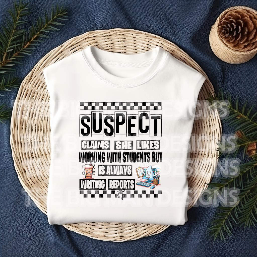May include: A tan sweatshirt with black text that reads 'SUSPECT CLAIMS SHE LIKES WORKING WITH STUDENTS BUT IS ALWAYS WRITING REPORTS' with a checkered pattern above and below the text. The text is surrounded by a black border.