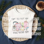 Folded white t-shirt on a wicker tray with the "Can't Talk Right Now Doing Teacher Stuff" design printed on the front.