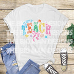 Flatlay of a white T-shirt with colorful "TEACH" design, paired with jeans and sneakers.