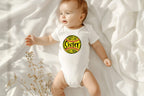 A lifestyle photo of a baby wearing a white baby onesie with a yellow softball graphic that says 'That's my sister out there'.
