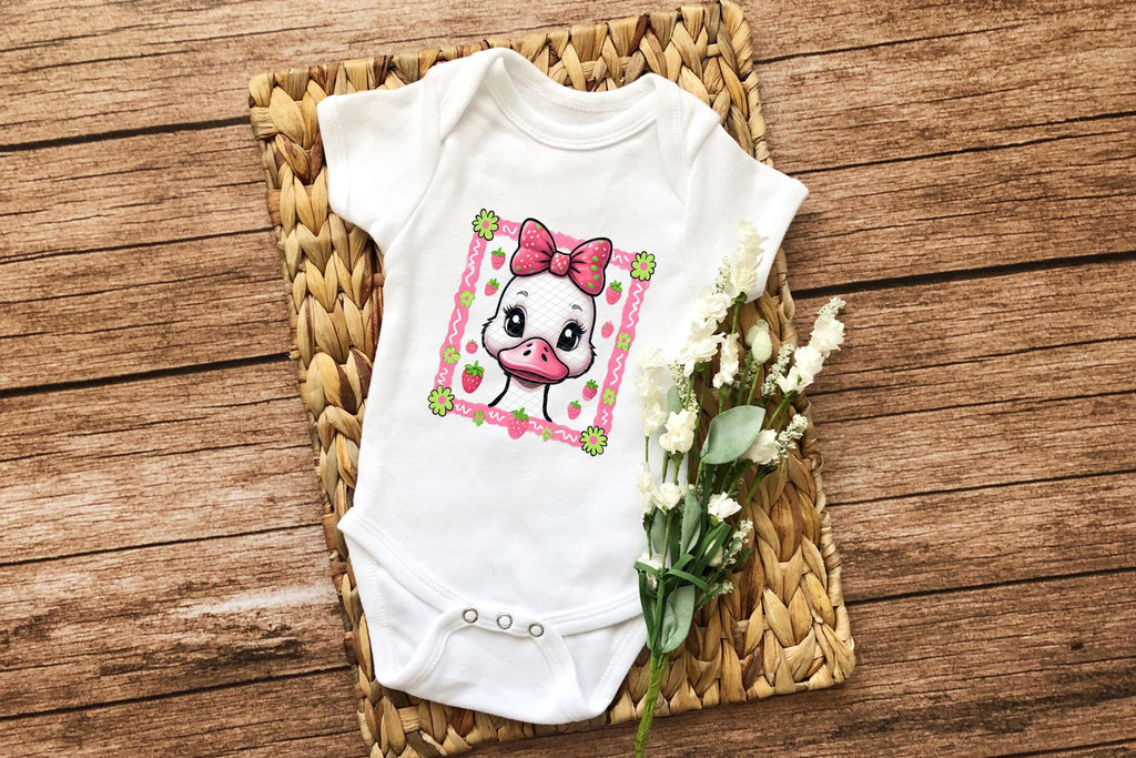 Baby onesie with pink bow duck print laying on wicker mat with white flowers.