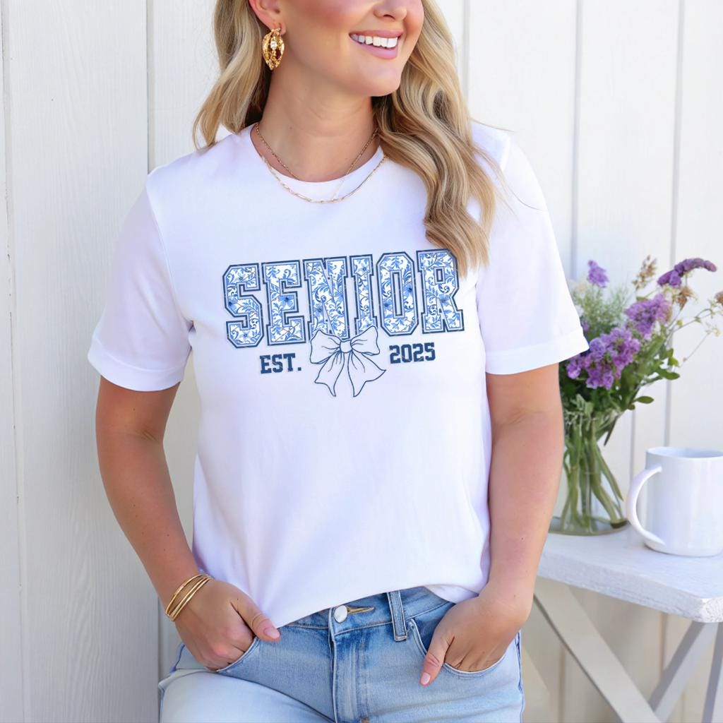 White T-shirt featuring "Senior Est. 2025" in floral blue print with a bow design, styled with jeans.