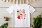 Close-up of toddler T-shirt featuring strawberry and bow design, decorated with rustic wood and plants.