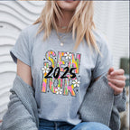 Woman wearing a grey Brushstroke Senior 2025 shirt, layered with a sweater and layered necklaces.