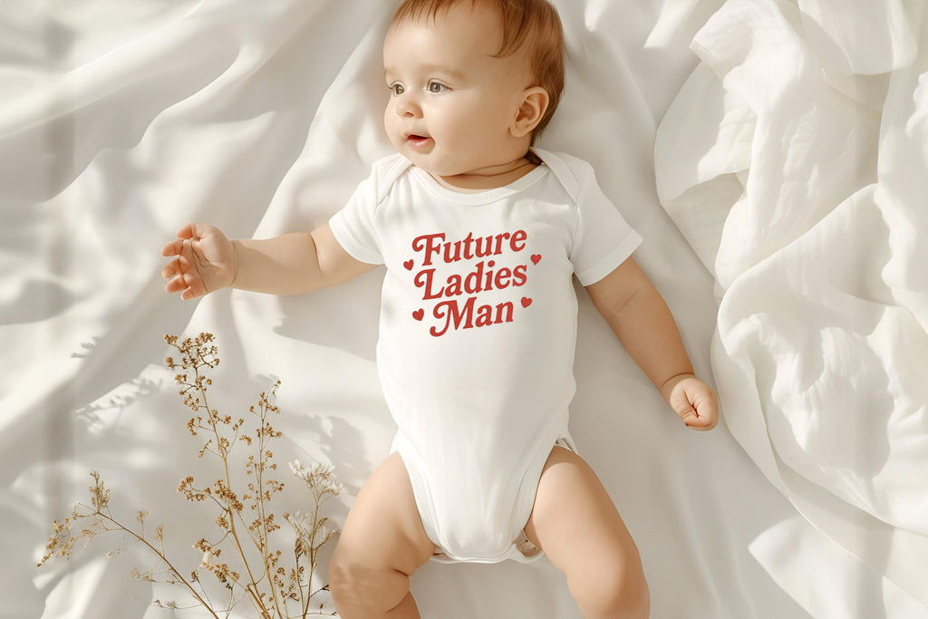 Baby lying on white blanket wearing "Future Ladies' Man" onesie with soft lighting