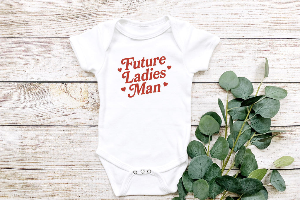 Close-up flat lay of onesie styled with eucalyptus leaves on light wood background