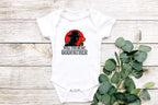 Flat lay with white wood background and eucalyptus leaves showcasing mafia-themed baby onesie.