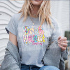 Woman wearing a sport grey t-shirt with colorful “Bruh We Out Teachers” design, layered with jewelry and cardigan, outdoor setting.