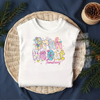 White t-shirt featuring “Bruh We Out Teachers” print folded neatly in a wicker basket with festive greenery decor.