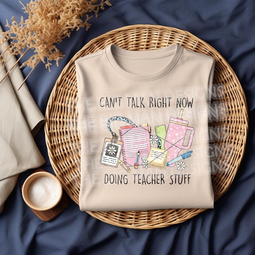 Folded natural sweatshirt displayed on a wicker tray with "Can't Talk Right Now Doing Teacher Stuff" graphic.