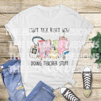 White t-shirt flat lay with jeans and sneakers, featuring "Can't Talk Right Now Doing Teacher Stuff" teacher graphic.