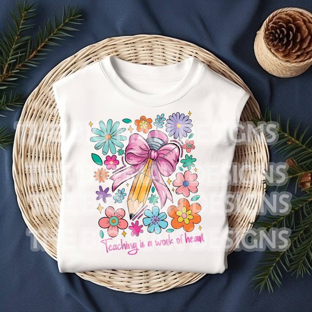 Folded white t-shirt with "Teaching is a Work of Heart" design surrounded by festive holiday greenery.