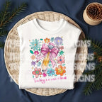 Folded white t-shirt with "Teaching is a Work of Heart" design surrounded by festive holiday greenery.