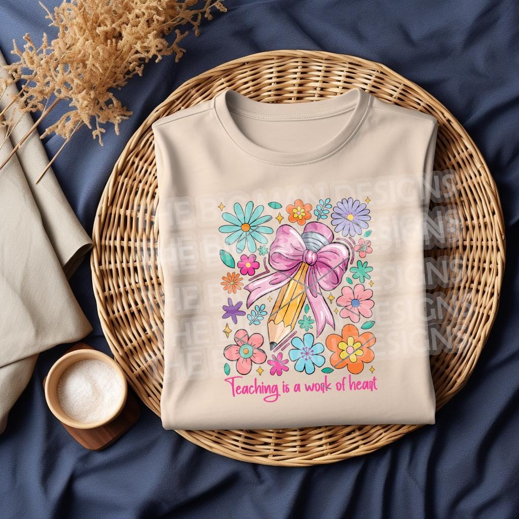 Folded natural sweatshirt with "Teaching is a Work of Heart" colorful pencil and floral design, styled on a wicker tray.