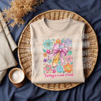 Folded natural sweatshirt with "Teaching is a Work of Heart" colorful pencil and floral design, styled on a wicker tray.