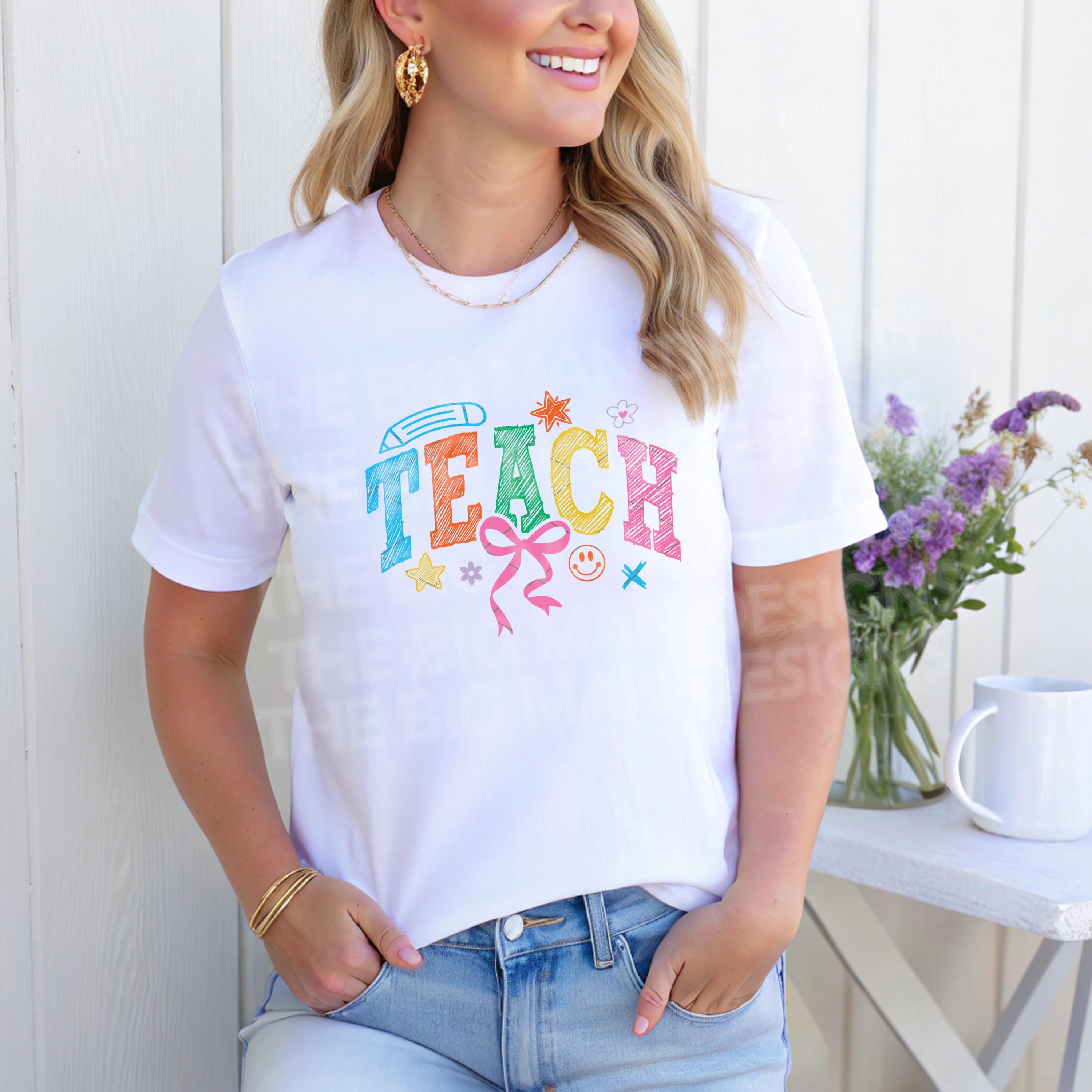 Woman standing wearing a white T-shirt with colorful "TEACH" design, smiling.