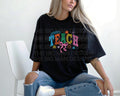Woman sitting cross-legged in a black oversized T-shirt with colorful "TEACH" graphic.