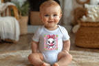 Baby sitting wearing silly goose onesie smiling in cozy living room.