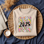 Flat lay of natural color Brushstroke Senior 2025 shirt in a wicker basket on navy background with cozy