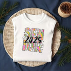 Folded white Brushstroke Senior 2025 shirt styled on a wicker basket with cozy holiday elements.
