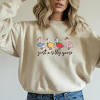 Funny goose sweatshirt in beige with colorful goose characters in dresses and text that reads ‘just a silly goose’
