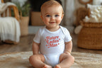 Baby boy sitting up smiling in white onesie with "Future Ladies' Man" text