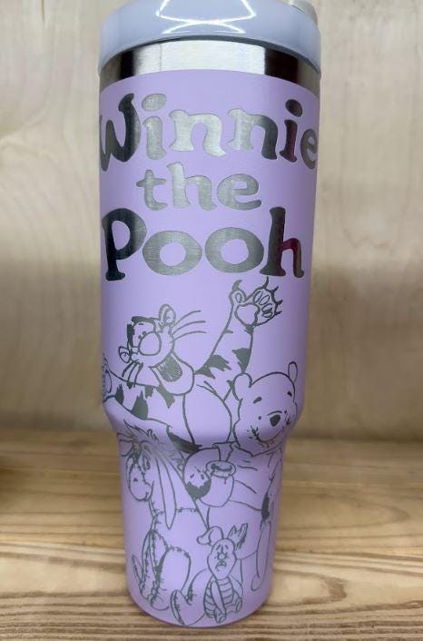 May include: A lilac stainless steel travel mug with a lilac handle and a clear lid. The mug has a silver design engraved into it.