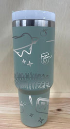 May include: A sage green stainless steel travel mug with a sage green handle and a clear lid. The mug has a silver design engraved into it.