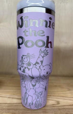 May include: A lavender tumbler featuring the words "Winnie the Pooh" in silver lettering. The tumbler has a white lid and a silver rim. The design includes illustrations of Winnie the Pooh and friends.